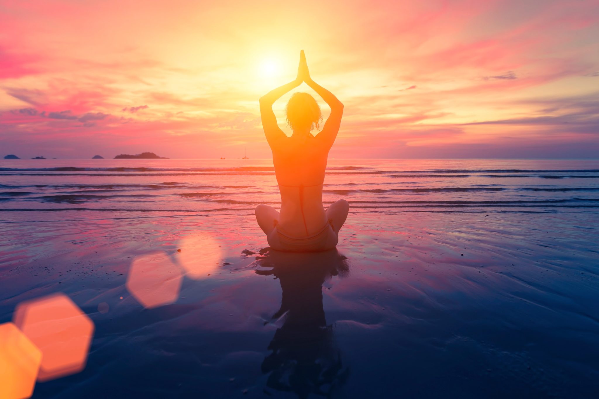 Femme en train de faire du yoga sur la plage au coucher du soleil.